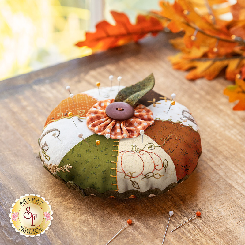 An orange, white, and green pin cushion with a small button topper on a wood table