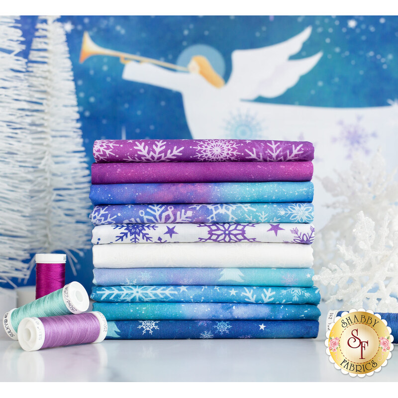 A stack of folded, colorful fabric featuring various snowflake patterns in shades of purple, blue, and white. Two spools of thread in complementary colors are placed beside the fabric, and a winter-themed background featuring a trumpet-playing angel is visible.