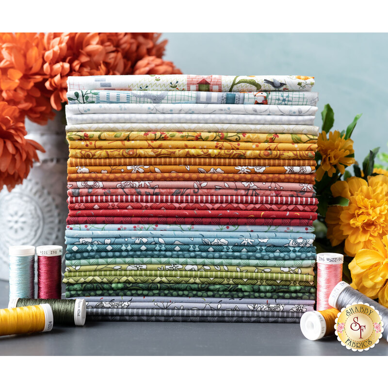 Photo of a stack of fabrics from the Wander Lane II collection with coordinating thread spools and flowers in the background.