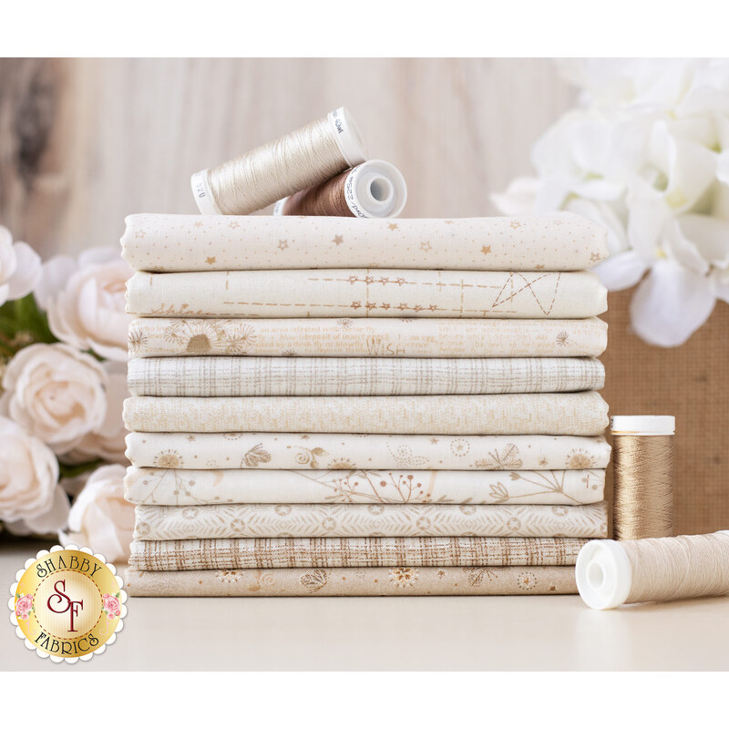 A stack of neatly folded fabric in various shades of cream and beige, with decorative patterns. Several spools of thread in coordinating colors are placed on top. In the background, there are soft pink flowers and a textured surface.