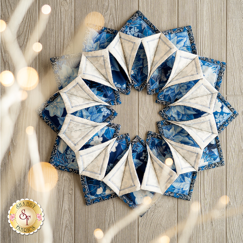 A circular arrangement of fabric pieces in various shades of blue, featuring floral patterns and triangular shapes. The design creates a star-like effect with alternating colors and textures.