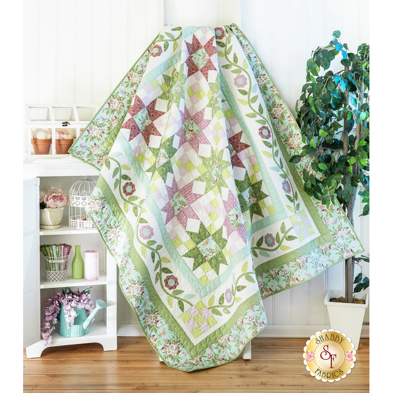 Quilt filled with sawtooth stars and flower appliqué in pastel green and purple colors.