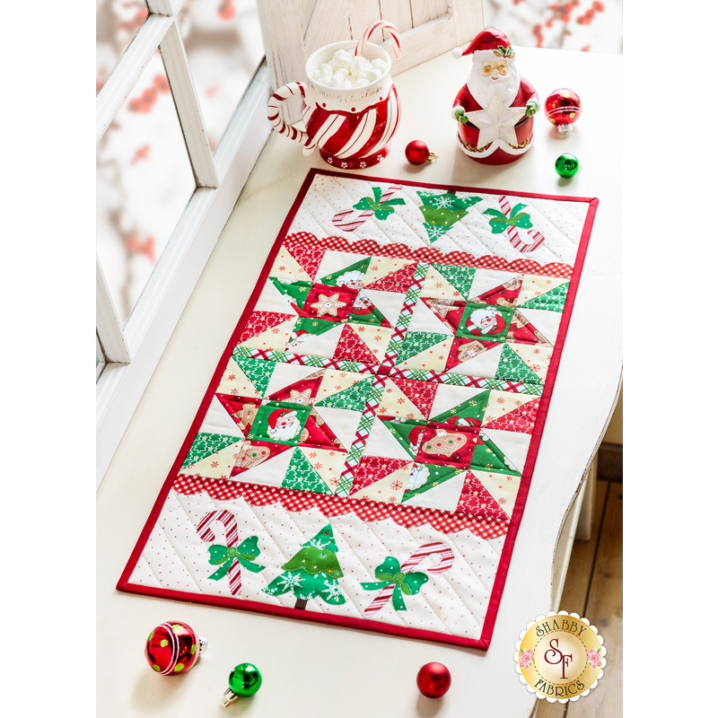 Table runner with triangle pinwheel design in Christmas themed Santa fabrics in red, white, and green.