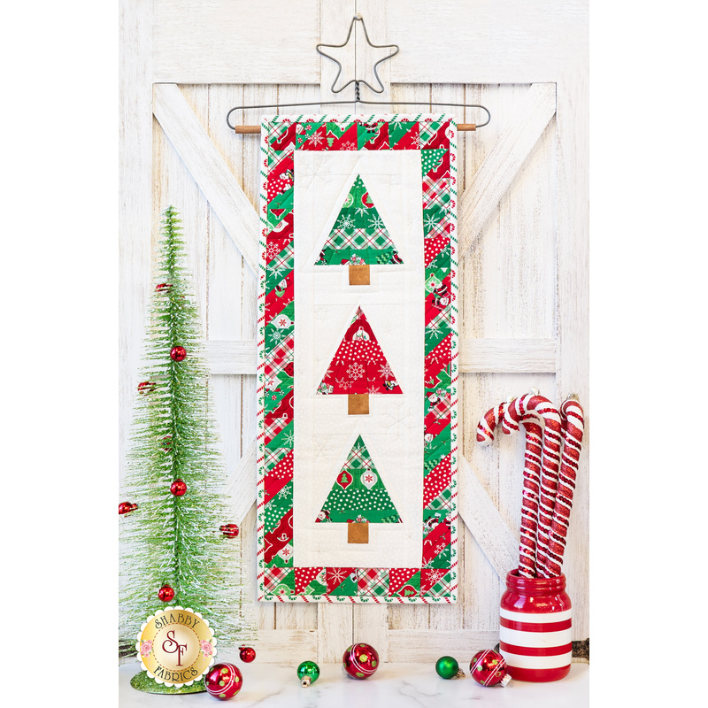 Small quilt with three pine trees in green, red, and white fabrics hanging from a star shaped craft holder.