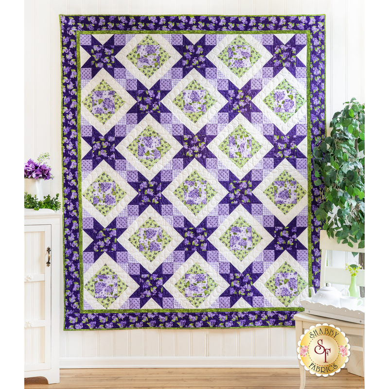 A quilt with sawtooth star design with geometric patchwork in Purple, white, and green floral fabrics.