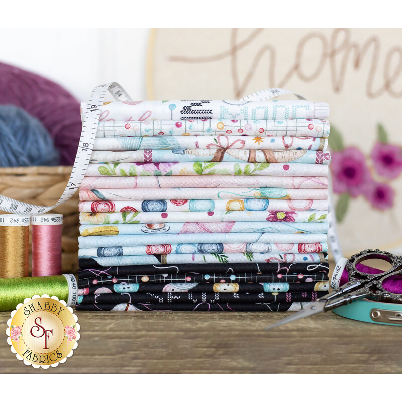 A photograph of stacked black, light blue, and white fabric with sewing motifs on a wood desk