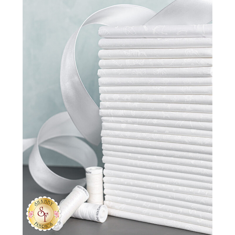 A neatly arranged stack of white fabrics is shown, with several spools of white thread and a flowing white ribbon positioned nearby. The background is a soft, light color.