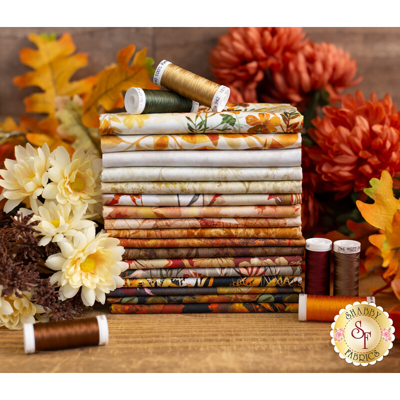 A stack of various fabrics in warm autumn colors and patterns, accompanied by spools of thread in shades of brown and gold, with flowers and leaves in the background.