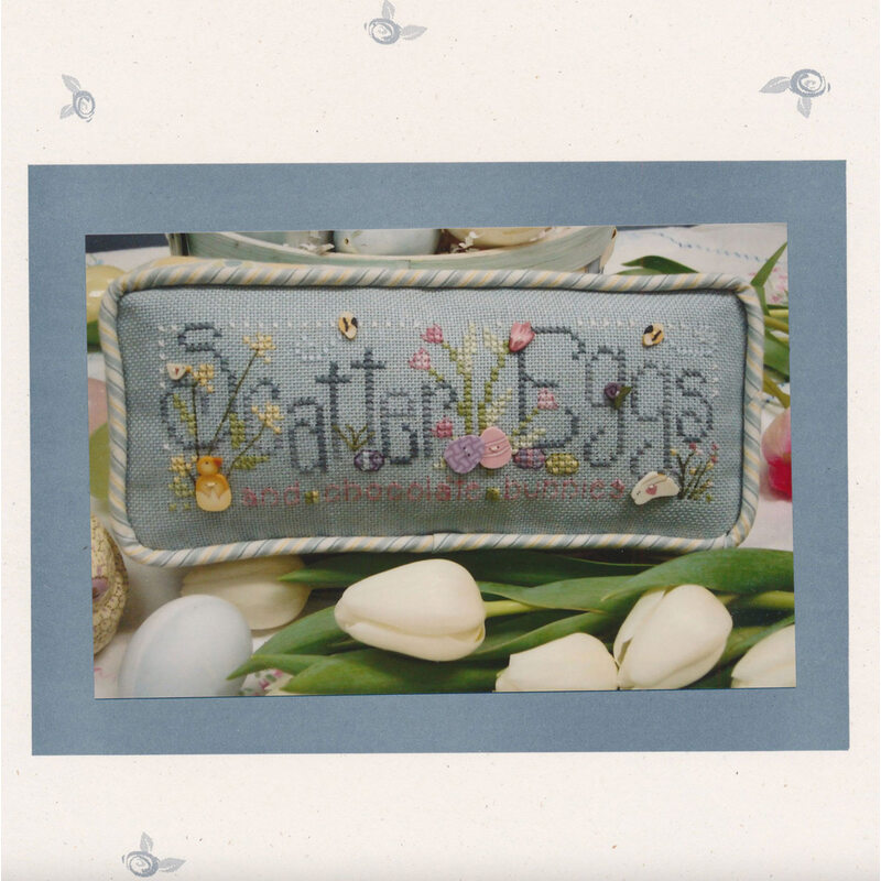 Picture of the scatter eggs cross stitch pattern, showing the finished pillow with the phrase and several easter buttons and symbols on it
