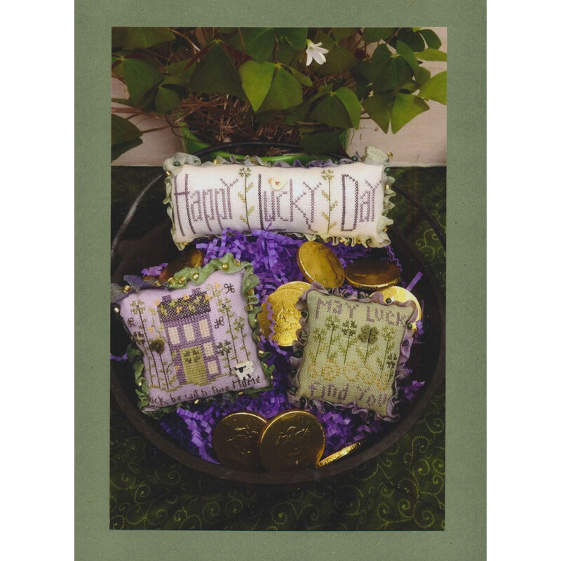 A decorative bowl filled with purple shredded paper, gold coins, and three cross stitched pillows with messages about St Patrick's Day.