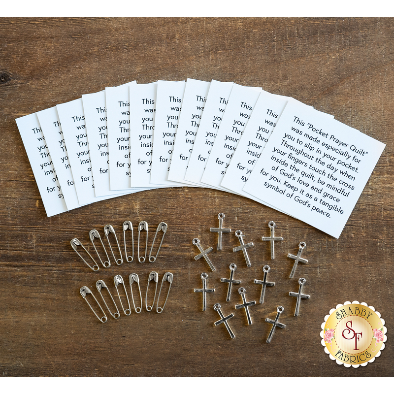 A collection of prayer cards and safety pins arranged on a wooden surface. The prayer cards contain text explaining their purpose, and there are several metallic crosses and safety pins scattered around them.