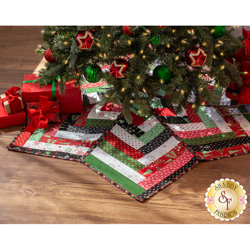 A festive tree skirt made with red, green, black, and white fabric strips under a decorated Christmas tree with wrapped gifts to one side.