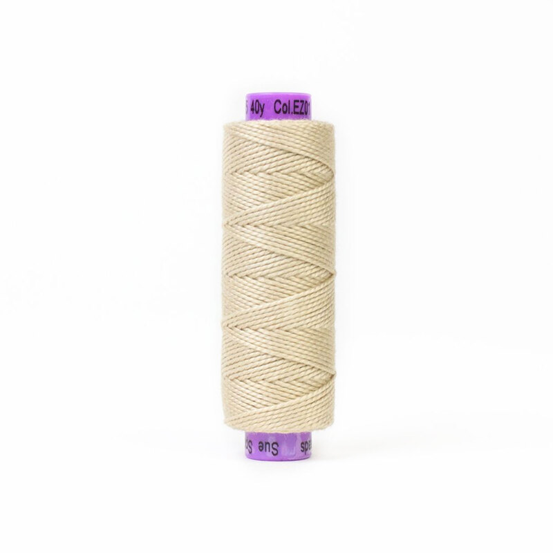 A spool of light beige sewing thread with a purple label at each end. The thread is wound evenly and displayed standing upright.