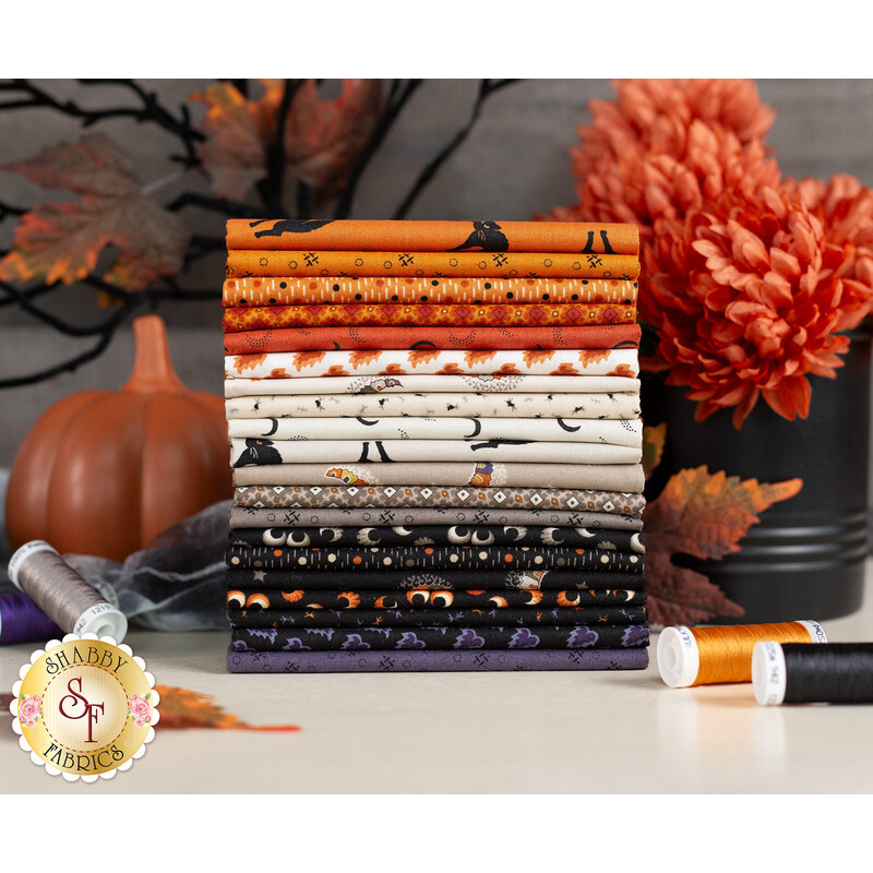 A stack of neatly arranged cotton fabrics in autumn colors, including orange, white, and black, with various Halloween-themed patterns. Nearby, there are a decorative pumpkin, colorful florals, and spools of thread.