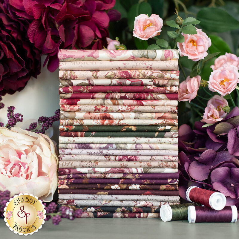 A stack of folded fabric rolls in various floral patterns sits among colorful flowers and spools of thread in shades of burgundy and cream.