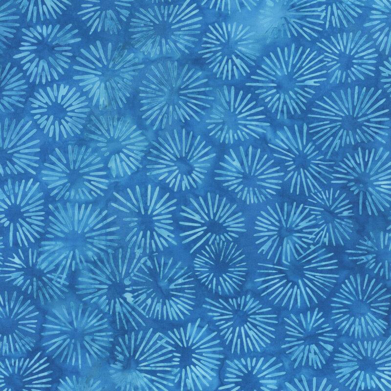 A blue mottled batik fabric with light blue sun bursts