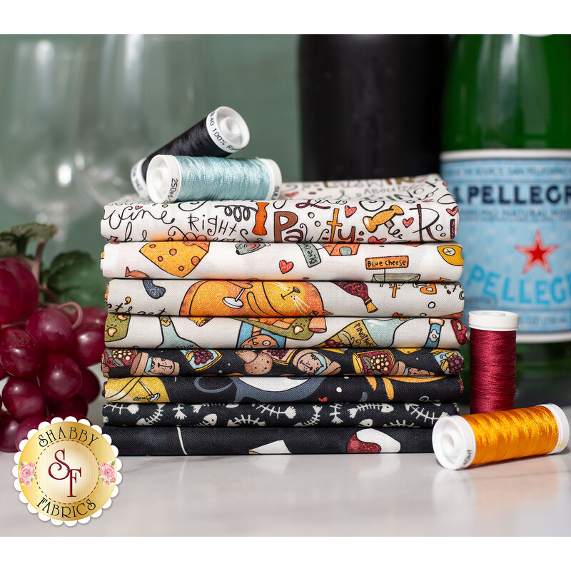 A stack of colorful fabric rolls featuring various patterns, alongside spools of thread in different colors, with a bottle of sparkling water and grapes in the background.