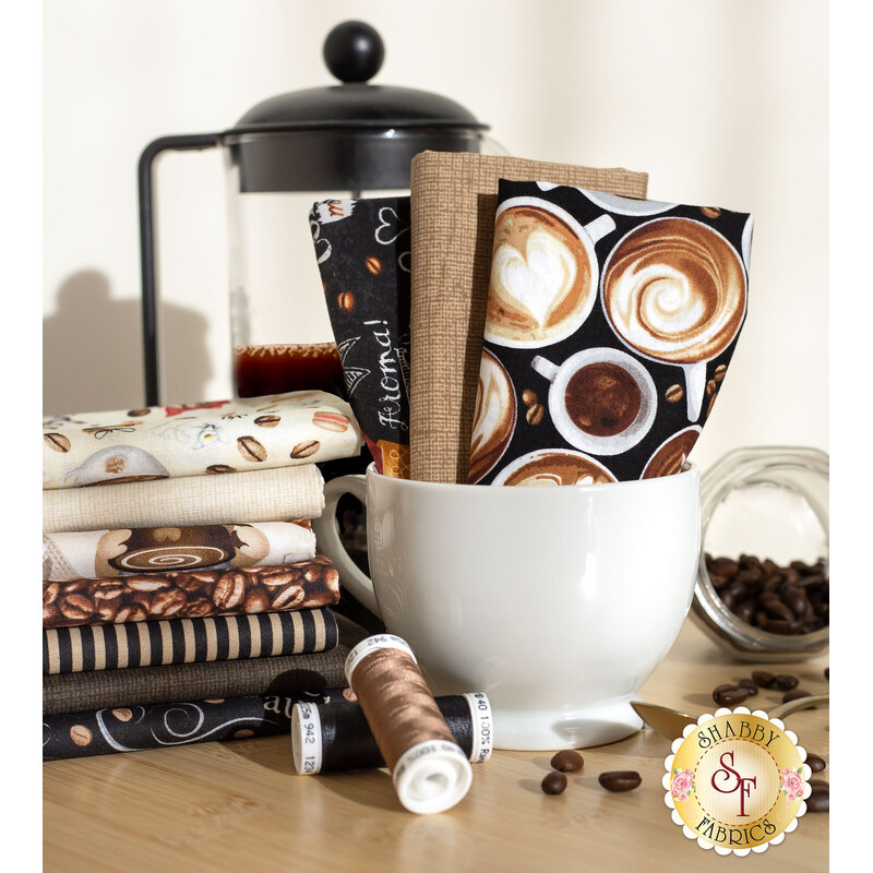 brown, black, and cream coffee related fabrics stacked in and around a coffee mug with coffee beans and a french press behind