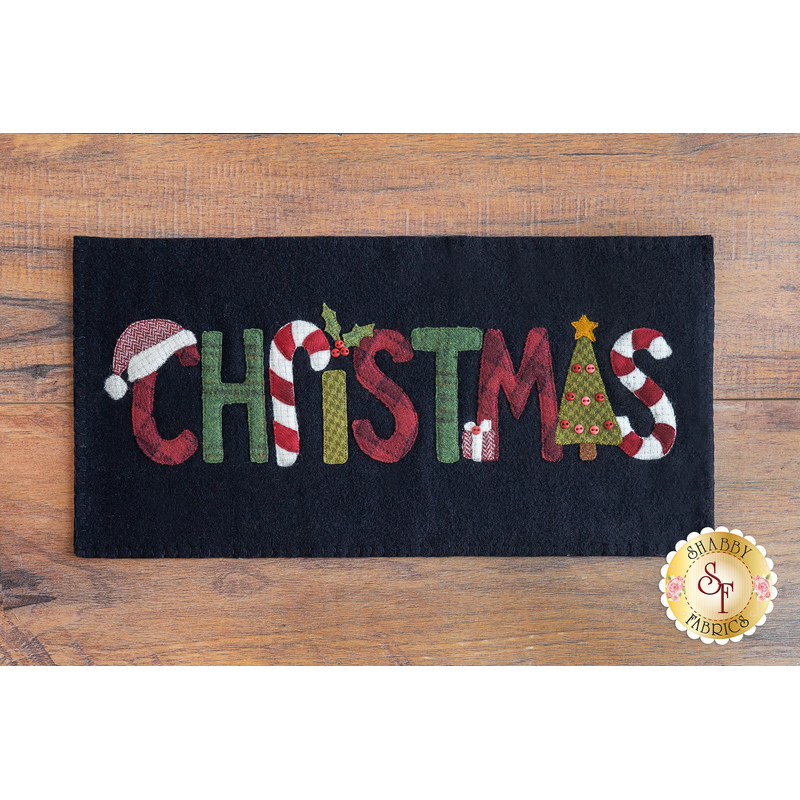 Black rectangular wool mat on a brown wooden countertop with the word 