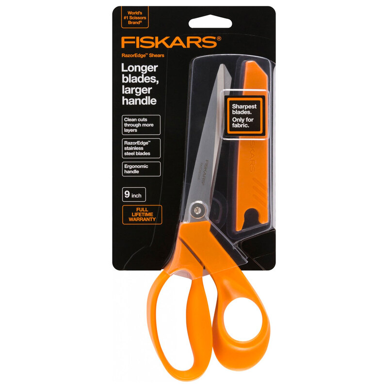 A package of Fiskars scissors featuring orange handles, labeled 9-inch, with a fabric-cutting note.