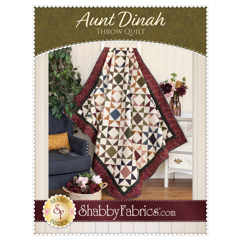Front cover of the Aunt Dinah Throw Quilt pattern showing a finished quilt draped in front of a white paneled wall with furniture and a houseplant