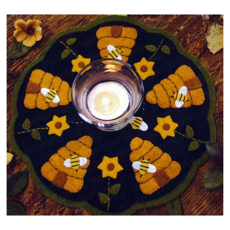 A circular decorative mat with a dark background featuring embroidered designs of beehives, bees, and flowers. In the center, there is a clear glass candle holder with a lit candle inside.