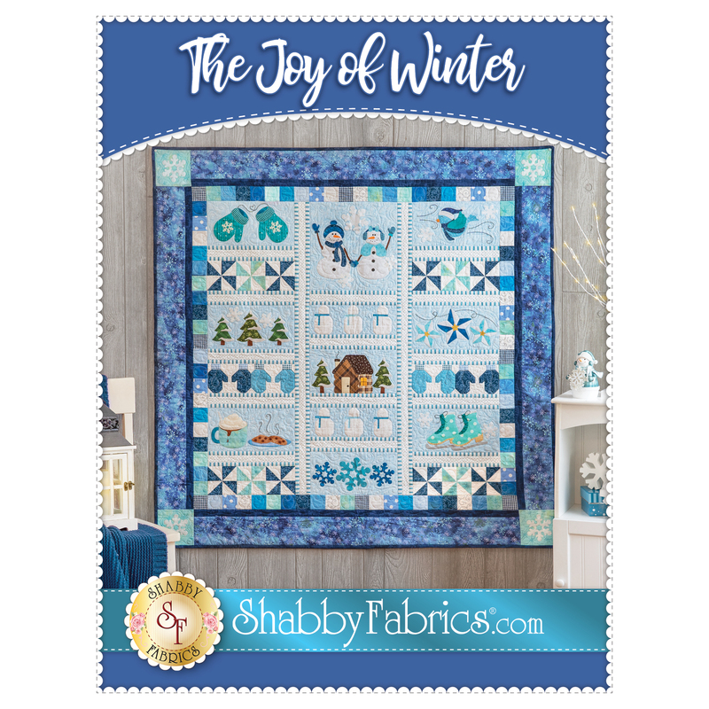 A decorative quilt titled The Joy of Winter featuring various winter-themed appliqués and designs, including snowmen, mittens, trees, and snowflakes, surrounded by borders in shades of blue. The quilt is displayed against a neutral wall with accent furnishings around it.