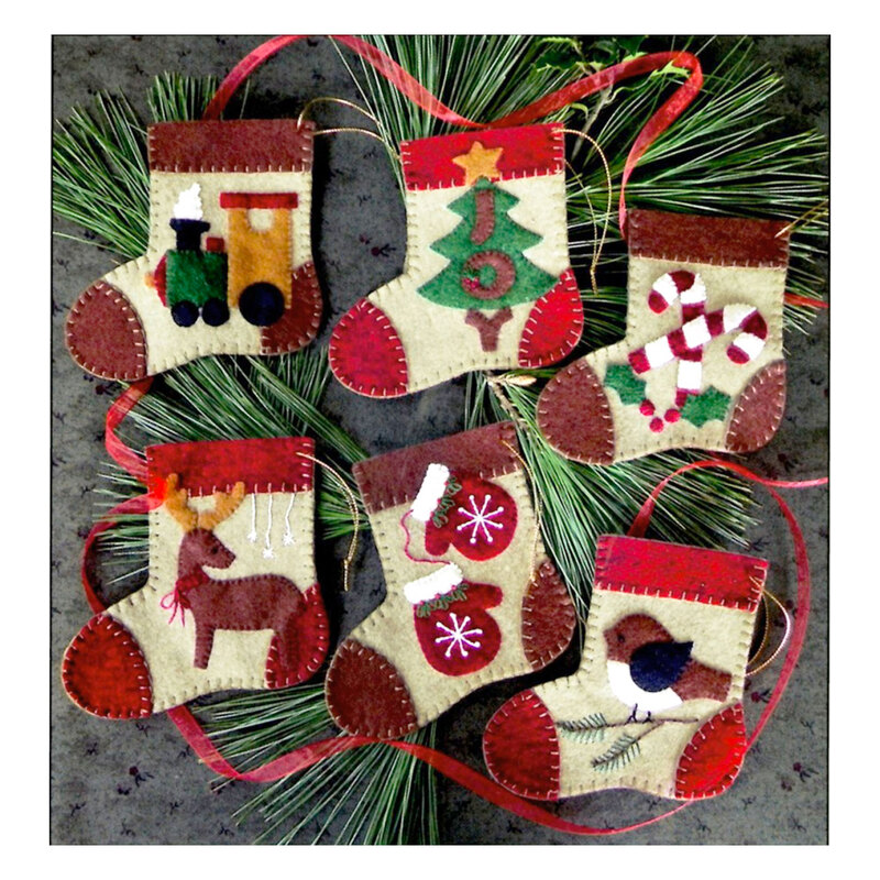 Photo of 6 mini stocking ornaments on a gray table top with pine tree boughs. Each stocking has a different motif including candy canes, mittens, and a train