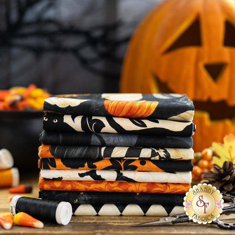 a photo of all fabrics in the Hallow's Eve FQ set, ranging from orange to cream to black staged with halloween decor