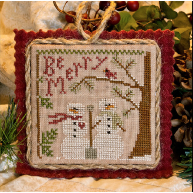 Front of pattern showing the completed small cross stitch ornament staged beside a pinecone atop a quilt