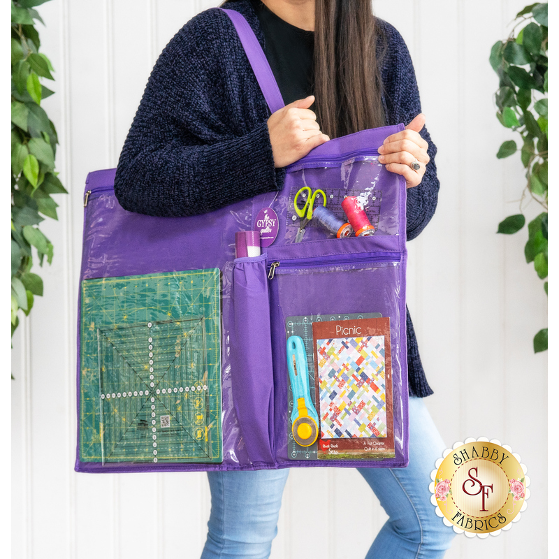 Close up image of someone holding the tote over one shoulder with the pockets filled with notions like thread spools and scissors for scale 