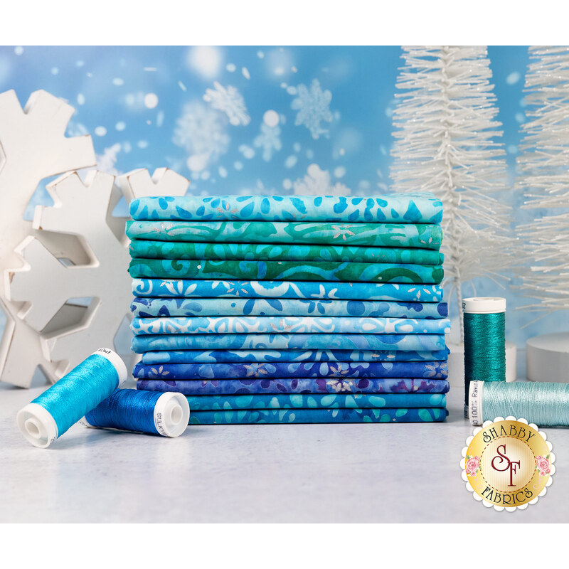 Stack of fabrics included in the the 13 FQ set, in front of an icy blue backdrop with blue, cyan, and turquoise spools of thread