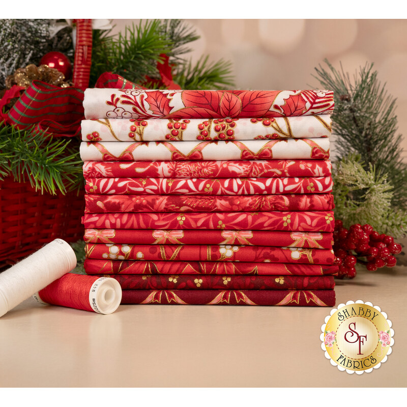 A stack of the fabrics included in the Holiday Flourish Festive Finery Red FQ set, with pine branches and a basket and thread.