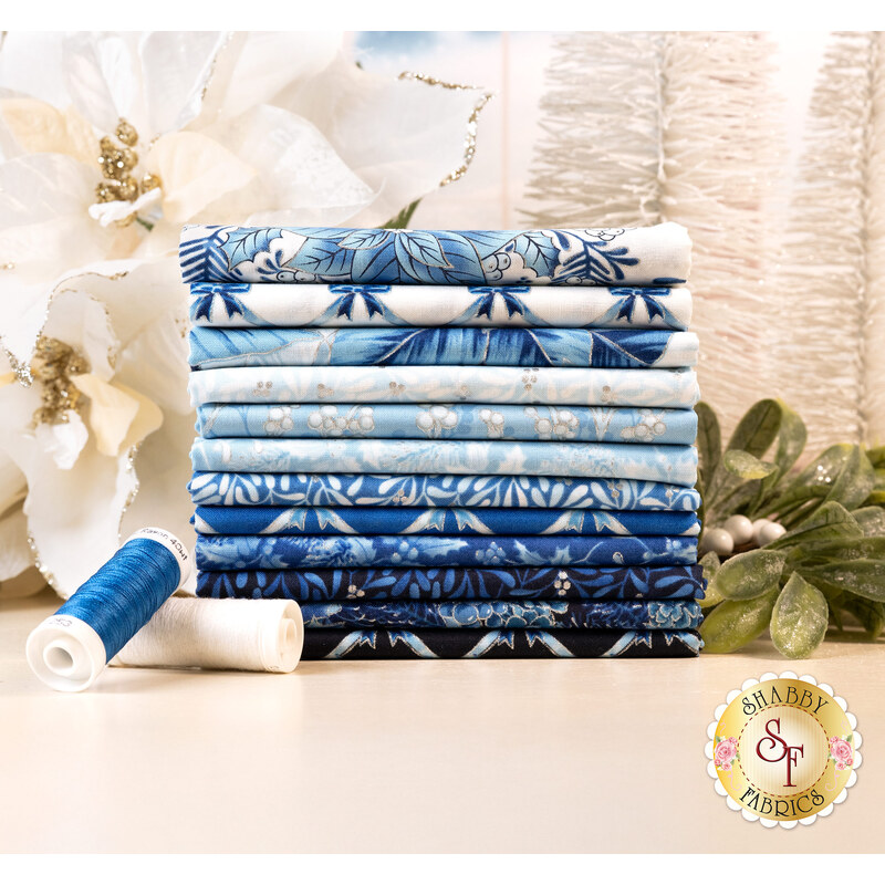 A stack of the fabrics included in the Holiday Flourish Festive Finery Blue FQ set, with trees and pointsettas and mistletoe and thread.