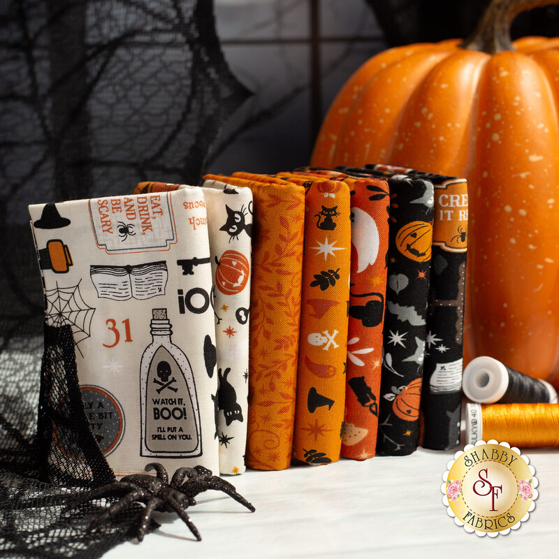 Stack of Halloween-themed fabric bundles in orange, black, and cream, with a decorative pumpkin.