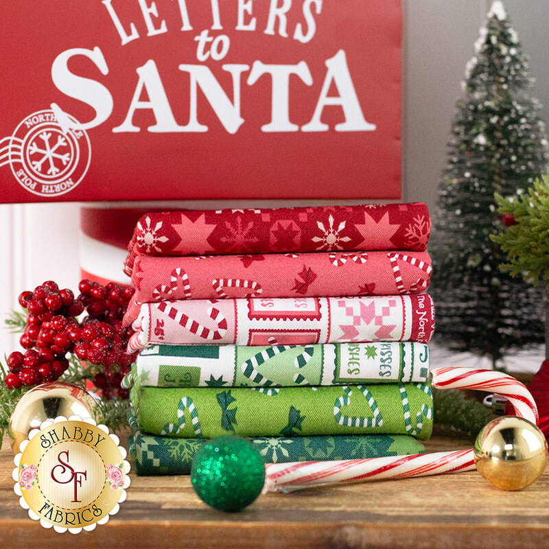 A stack of festive fabrics in red, green, and white with Christmas patterns, beside holiday decorations.