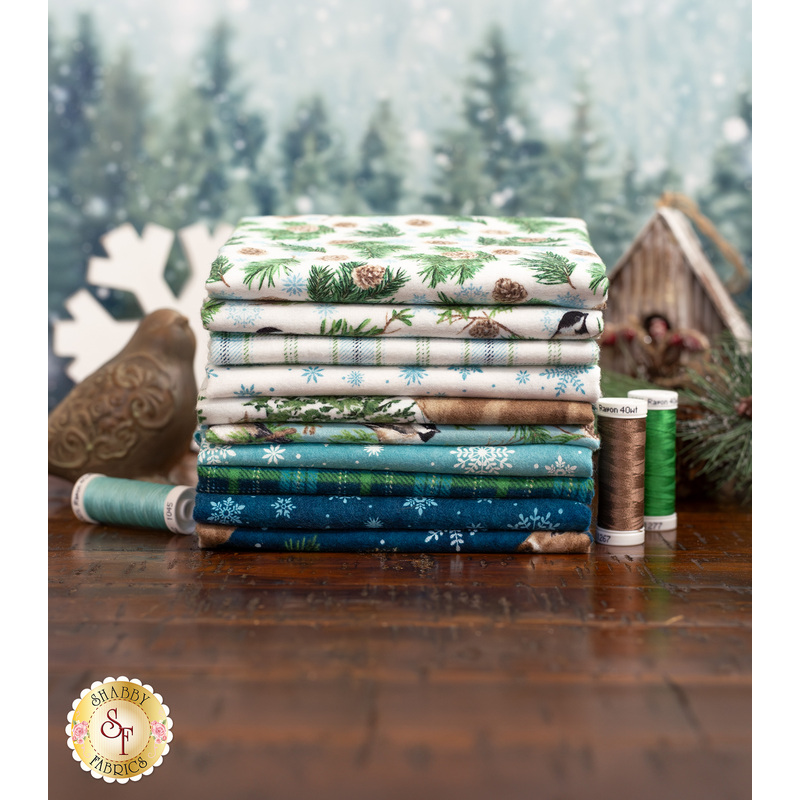 Stack of patterned fabrics featuring pinecones and snowflakes, with spools of thread beside them.