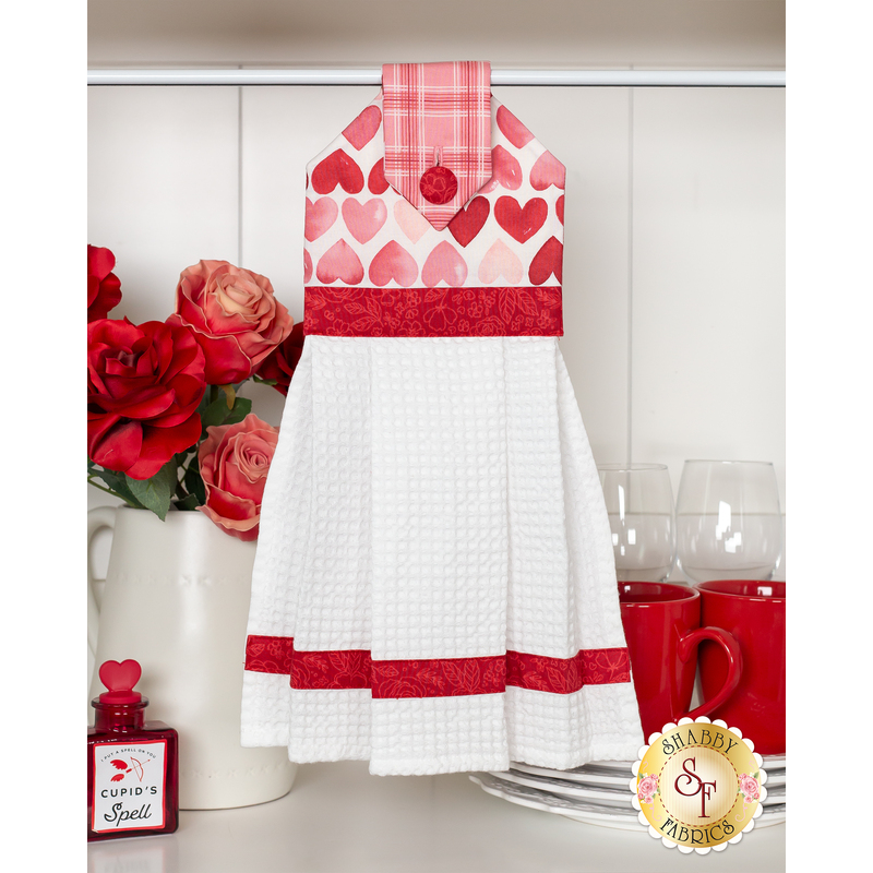 The completed hanging towel staged with red roses, red mugs, and white kitchenware.