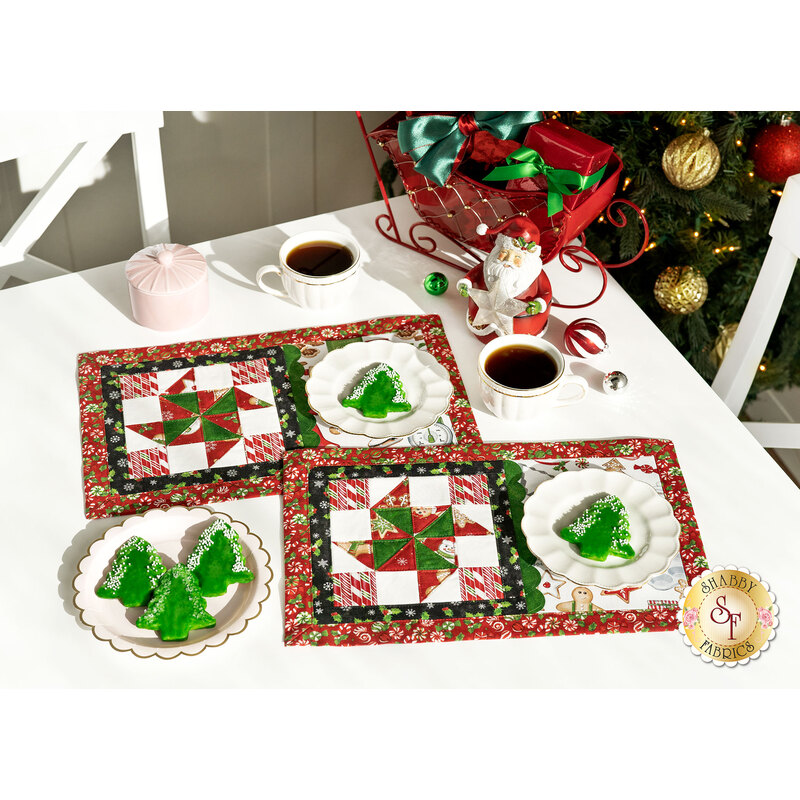 The two completed placemats for December, colored in bright festive colors and paired with coordinating Christmas decor, staged on a white table with tea ware.