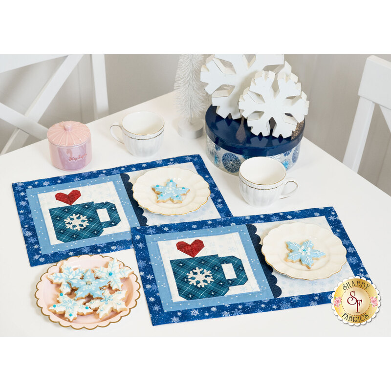 The two completed placemats for January, colored in cool winter fabrics and paired with coordinating decor, staged on a white table with tea ware and snowflake cookies.