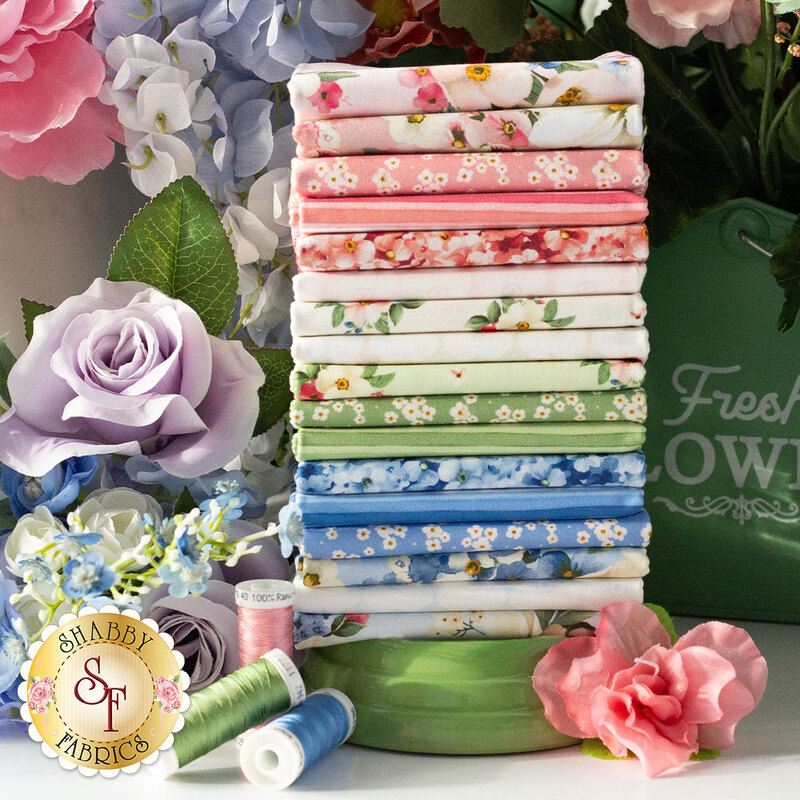 Stack of seventeen colorful floral cotton fabrics surrounded by artificial flowers and spools of thread.