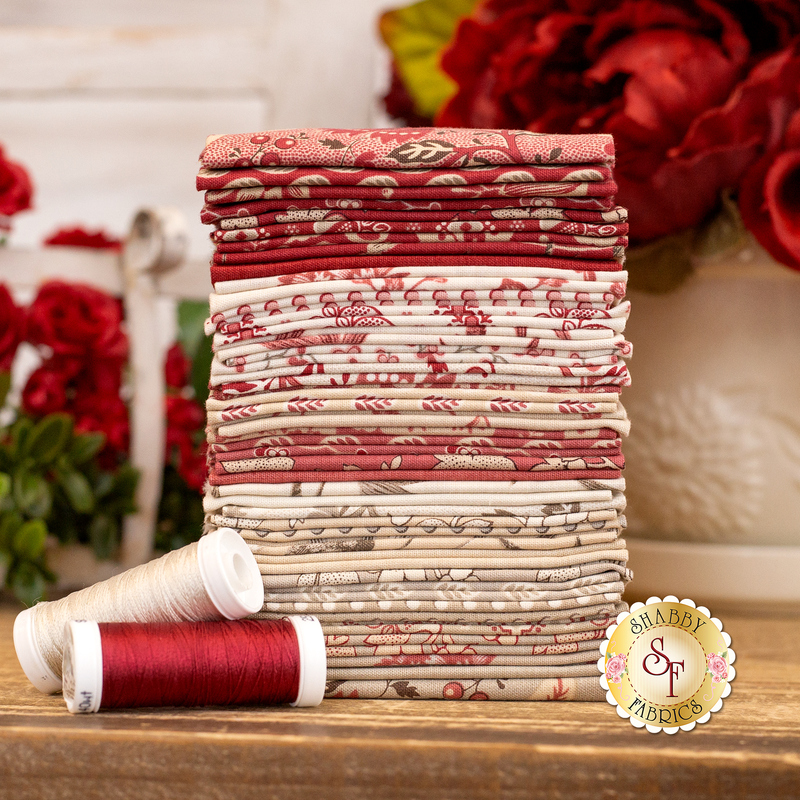 A photo of a stack of fabrics in Rouenneries Trois FQ Set in red, pink, gray, and cream set next to roses and thread spools