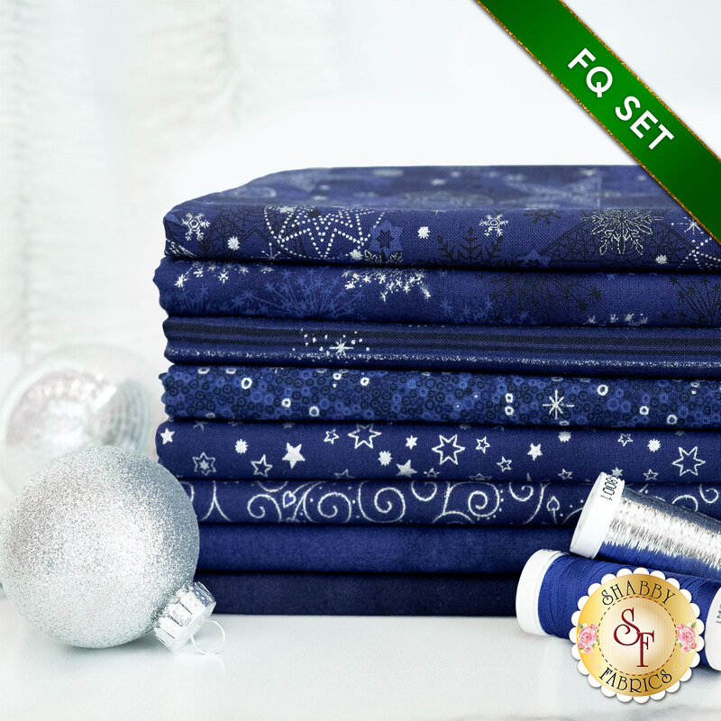 A photograph of the stacked fat quarters included in the Dark Blue/Silver set, staged with blue and silver thread and silver ornaments.