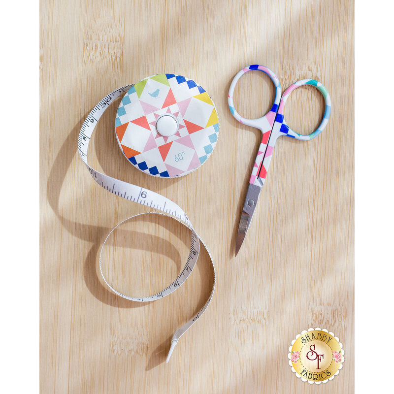 A colorful measuring tape rolls beside a pair of decorative scissors on a wooden surface.