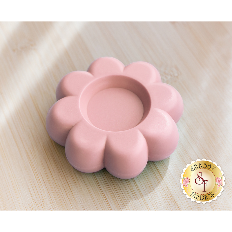 A pink flower-shaped magnetic dish with a central indentation, set on a wooden surface.