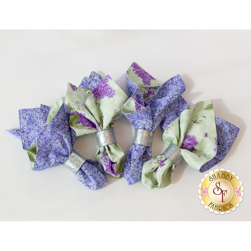 The four reversible Bloomerang cloth napkins fastened with silver napkin rings and isolated on a white background. A golden Shabby Fabrics logo can be seen in the lower right hand corner.