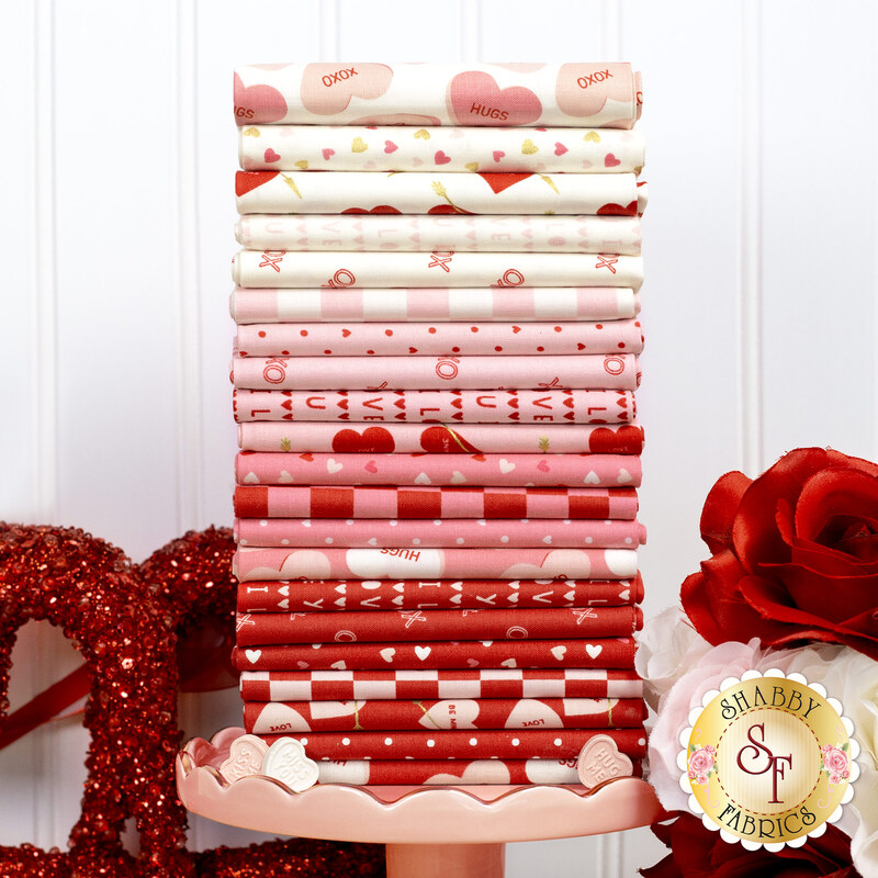 A stack of white, pink, and red fabrics included in the Sweetheart FQ Set, with flowers and hearts.