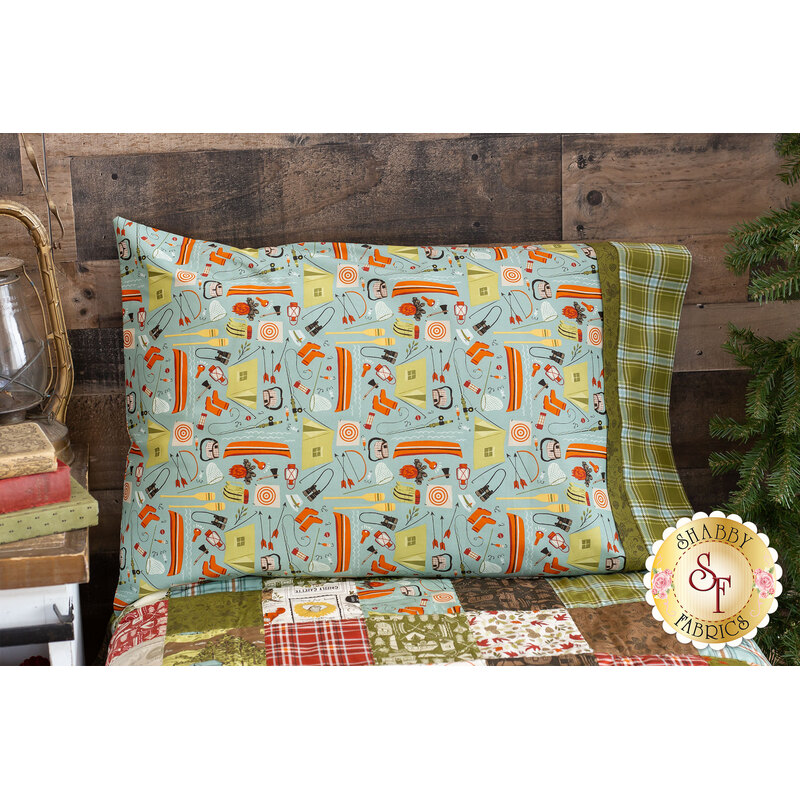 A shot of the Magic Pillowcase in Blue, staged on a bed with a matching patchwork quilt in a cabin setting.