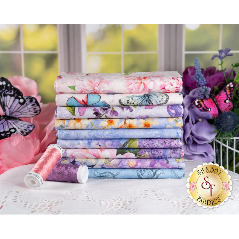 A stack of the fabrics in the Secret Garden collection, with flowers and butterflies and thread.