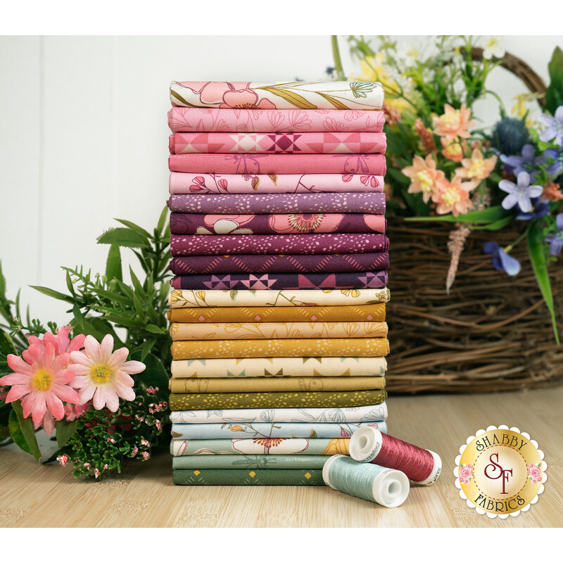 A stack of the fabrics for Meadow Walk, with flowers and a basket and thread.